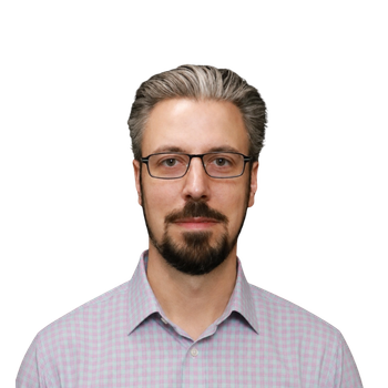 Man with glasses and short, slicked-back gray and brown hair, a beard, and mustache, wearing a light-colored checkered shirt, against a plain white background.