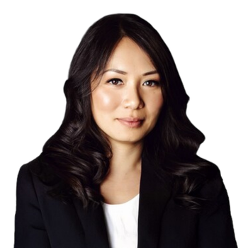 A woman with long, wavy black hair wearing a black blazer and white top, posing against a plain light background.