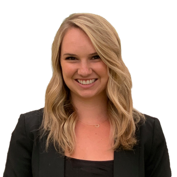 A woman with long blonde hair wearing a black blazer and top smiles at the camera against a plain white background.