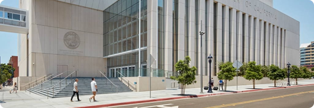 A modern courthouse building with tall windows and a wide staircase; a few people are walking on the sidewalk outside.
