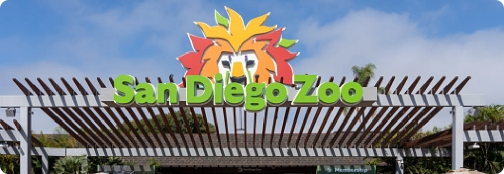 Entrance sign for the San Diego Zoo with green lettering and a stylized lion face above the text, set against a blue sky.