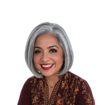 Smiling woman with straight gray hair in a bob cut, wearing a maroon top with floral embroidery, posing against a plain white background.